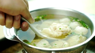 手里拿着一把勺子，在碗里盛着馄饨汤和葱。视频素材模板下载
