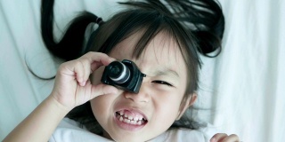 可爱的小女孩周末在床上玩相机，带着积极的情绪