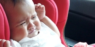 悲伤的婴儿在驾驶途中在红色的汽车座椅上哭泣