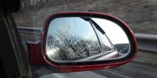 在一辆行驶中的汽车后视镜里拍摄早春的景色