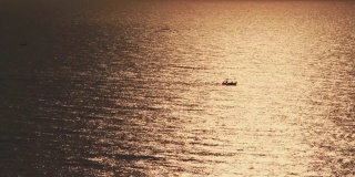 海面上的渔舟在日出或日落中发出金光的剪影