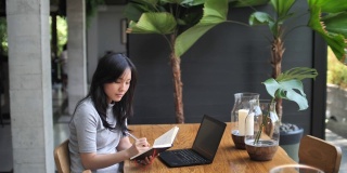 亚洲女人在咖啡馆工作，一边喝咖啡一边写笔记，自由职业