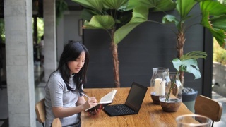 亚洲女人在咖啡馆工作，一边喝咖啡一边写笔记，自由职业视频素材模板下载