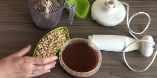 一个女人在一个搅拌花生和葵花籽的碗里睡着了。容器旁边是蜂蜜。烹饪halva的原料。