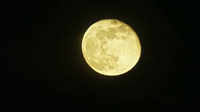 当一架喷气式飞机在月亮和照相机之间飞过时，一个巨大的、接近满月的月亮(渐亏的凸月)发出黄色的光芒