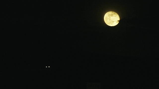 一个接近满月(渐亏的凸月)在州际公路上闪烁着黄色的汽车前灯和尾灯