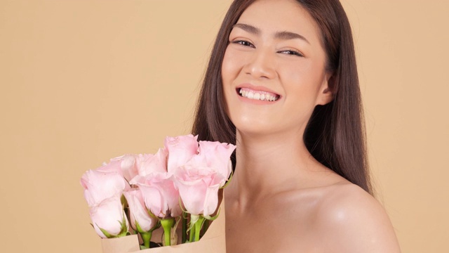 美丽的亚洲女人的肖像看着相机迷人的微笑。美丽的亚洲女人手里拿着玫瑰与幸福的情感。具有美容护肤理念的人。