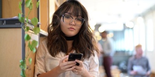 年轻的亚洲女商人在现代共同工作空间使用手机的肖像