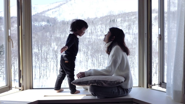 一个孩子和他的母亲在窗前亲吻，看着森林里的雪花飘落。