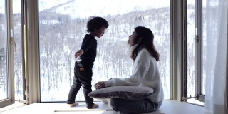 一个孩子和他的母亲在窗前亲吻，看着森林里的雪花飘落。