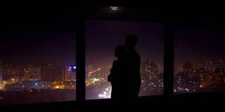 这对情侣在夜色中的城市背景下，靠近窗户拥抱。时间流逝