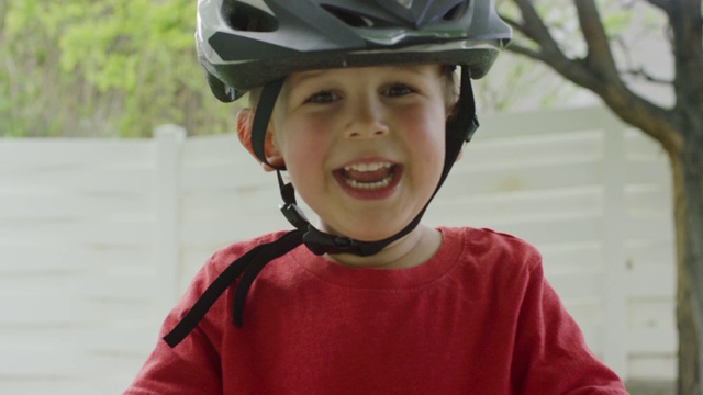 一个可爱的三岁白人男孩戴着自行车头盔，站在他的自行车旁边，在户外笑