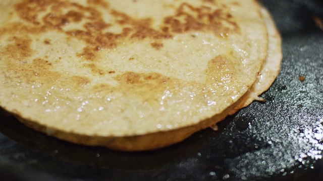 一个人用一个金属烙饼翻转一个墨西哥粉饼(玉米饼和奶酪)在一个铸铁煎锅在炉灶上烹饪