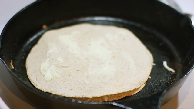 一名白人妇女的手用餐刀在玉米饼上涂上黄油，然后把它放在炉灶上的铸铁煎锅里油炸玉米饼上