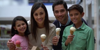 一对漂亮的夫妇和他们的两个孩子在购物中心微笑着面对镜头享受冰淇淋