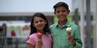 可爱的姐妹俩在商场里对着镜头微笑，手里拿着冰淇淋，互相拥抱