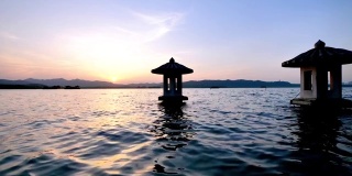 中国杭州西湖美丽的夕阳景观，橘色的黄昏天空和宁静的水与湖中的传统亭台楼阁，闪烁的涟漪，4k电影，慢镜头。