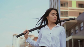 日本女孩看着镜头，站在风与传统武士刀。视频素材模板下载