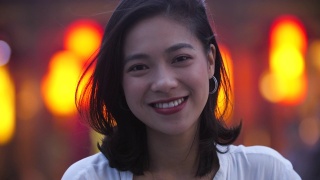 夏城的夜晚，一名年轻的亚洲女子对着镜头微笑，4k美元视频素材模板下载