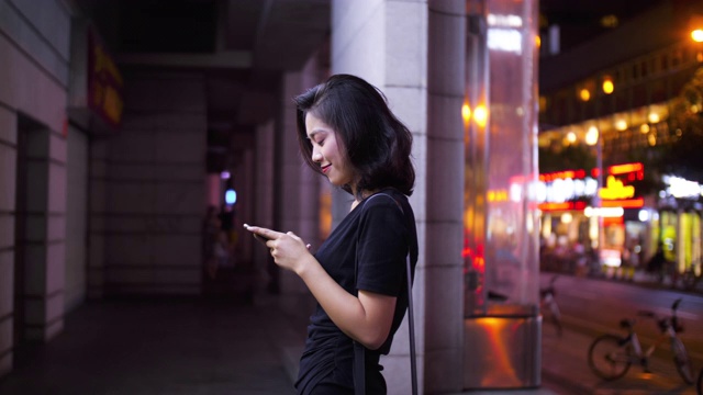 侧面的可爱的年轻亚洲女人使用手机在街上
