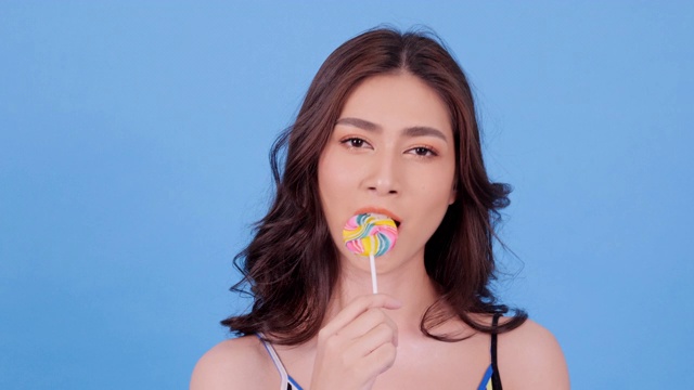 美丽的亚洲女人吃糖果与幸福的情绪在蓝色的背景。美丽，时尚和夏天的概念。