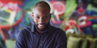 千禧黑人男性创意在工作场所的壁画前对着镜头微笑，头和肩膀