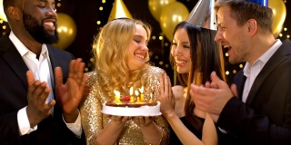 快乐的金发女人吹蛋糕蜡烛，朋友祝贺女人生日