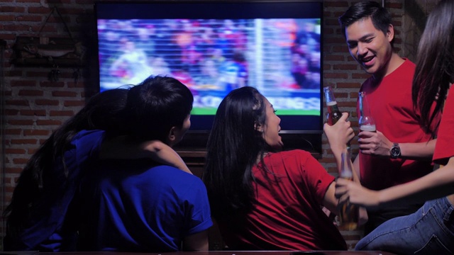 不同的亚洲朋友群在体育酒吧看电视。他们队进了一球，赢了。兴奋的朋友一边看足球比赛一边在酒吧喝啤酒。当他们喜欢的球队得分时，他们都欢呼。快乐的年轻人。