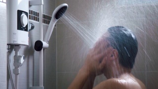 年轻的亚洲男人在浴室里用淋浴洗澡，充满新鲜感。视频素材模板下载