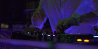 在夜总会派对上，男DJ在音响上播放舞曲。夜总会混合音乐和彩色灯光的DJ控制器。舞会上的音乐播放台和调音台