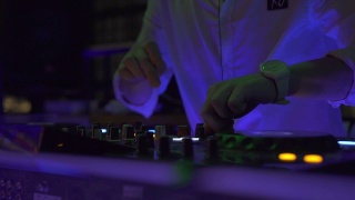 在夜总会派对上，男DJ在音响上播放舞曲。夜总会混合音乐和彩色灯光的DJ控制器。舞会上的音乐播放台和调音台视频素材模板下载