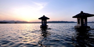 美丽的日落风景在西湖，中国，杭州，橘色的黄昏天空和宁静的水与传统的亭台楼阁在湖中，闪烁的涟漪，超级慢的动作。