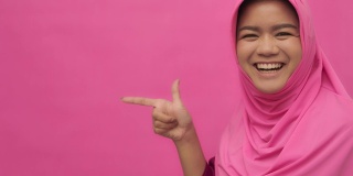 SLO MO穆斯林妇女的肖像与手势指向你的标志粉红色的背景拷贝空间