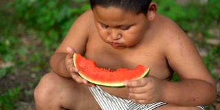 快乐的亚洲胖男孩在户外吃西瓜