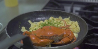 红蟹和意大利面在厨房炉子上的煎锅里烹饪。厨师在餐厅厨房的平底锅里将调料洒在意大利面上。用新鲜海鲜烹制意大利面