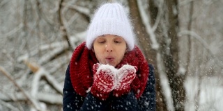 年轻的姑娘戴着白色的针织帽，戴着红色的围巾和手套吹雪