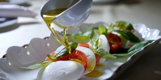 健康食品和素食的概念。在卡普里沙拉上倒入橄榄油的特写。意大利马苏里拉芝士沙拉。慢动作