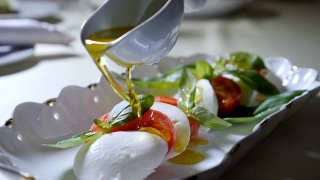 健康食品和素食的概念。在卡普里沙拉上倒入橄榄油的特写。意大利马苏里拉芝士沙拉。慢动作视频素材模板下载