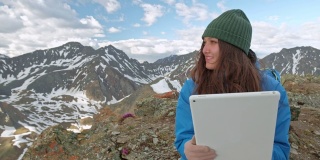 女自由旅游者在大自然中使用电脑，坐在草地上，旁边是燃气手电筒。山脉反射在笔记本电脑的屏幕上