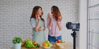 两个年轻的亚洲女性美食博主拿着红苹果，一边讲解健康的食物和健康的生活方式，一边录制视频播放，Vlog健康的生活方式