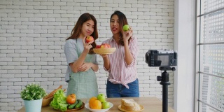 两个年轻的亚洲女性美食博主拿着红苹果，解释健康的饮食和健康的生活方式，同时录制视频供广播，Vlog健康的生活方式