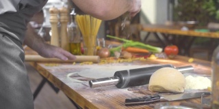 厨师厨师一边用擀面杖擀面，一边在披萨面团上撒面粉。男子在意大利餐厅为新鲜的意大利面制作面团。自制糕点、蛋糕和派。自制的健康食品