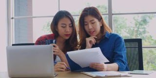 两个年轻的亚洲女性工作文书工作和喝咖啡在家办公室与幸福，办公室休闲的生活方式