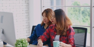 两个年轻的亚洲女性工作与电脑和喝咖啡在家庭办公室与幸福，办公室休闲的生活方式