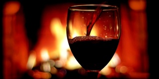 红酒被倒进豪华的空杯子与舒适温暖的壁炉在一个黑暗的公寓室内背景的特写拍摄