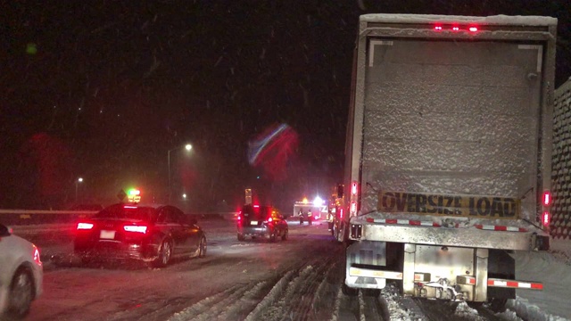 在暴风雪的夜晚，在州际公路上被事故和紧急救援人员拦下时，从一辆车的前面拍摄的