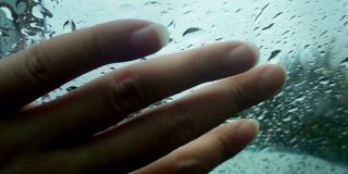 女性的手触摸着玻璃上的雨滴。触觉