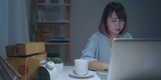 美丽聪明的亚洲年轻企业家女企业家企业主中小企业网上检查产品库存和保存到电脑工作到深夜在家里。小企业主在家办公的概念。