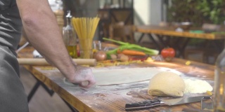 一名男子在厨房的桌子上为意大利面滚动新鲜的面团。厨师用擀面杖擀薄饼。自制糕点、蛋糕、披萨和意大利面。做手工制作的食物