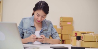 聪明的亚洲年轻企业家女企业家企业主中小企业在线检查产品库存和保存在手机上工作在家里。小企业主在家办公的概念。